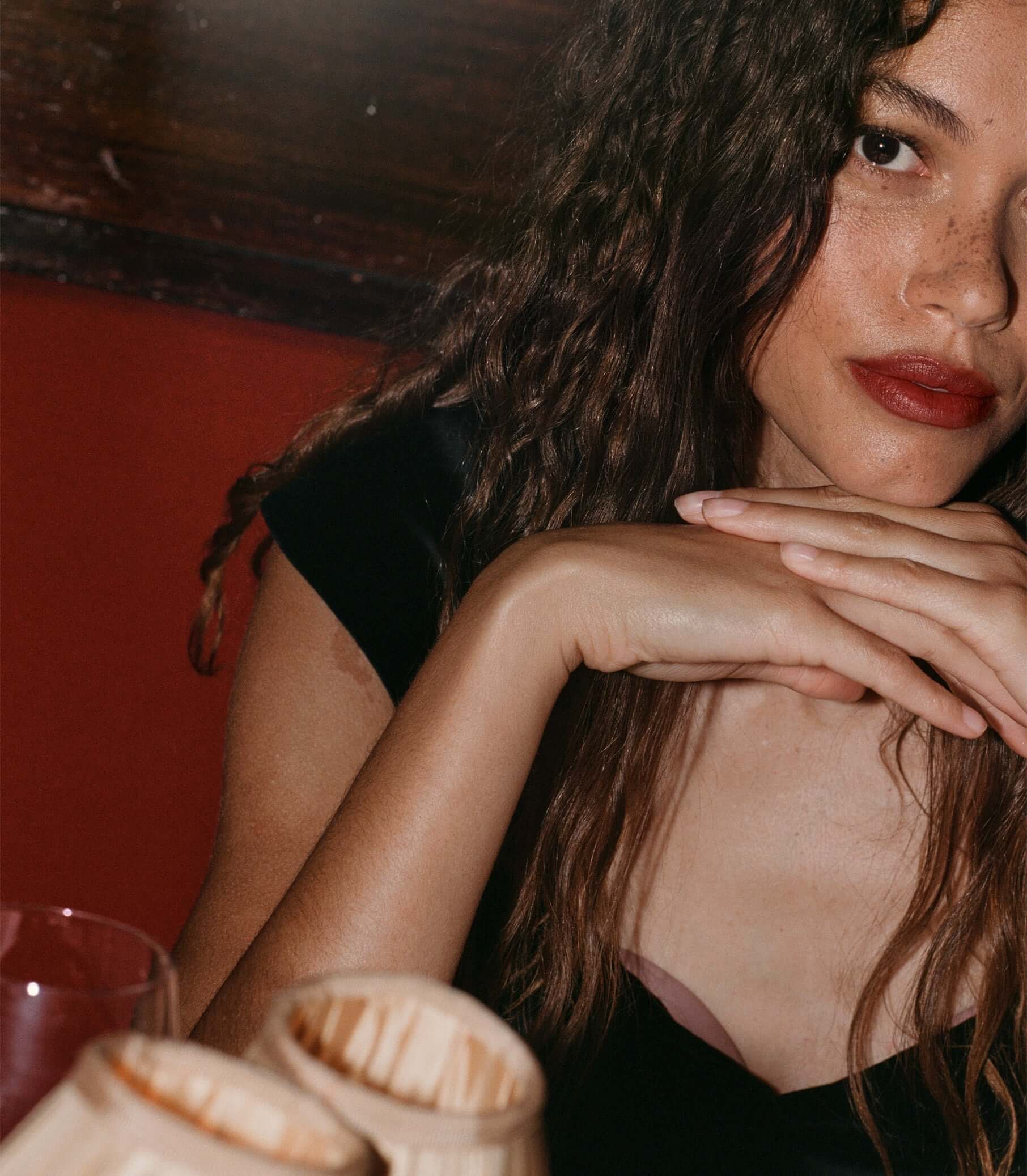 A stylish woman with long hair and red lips showcasing accessories on a table.